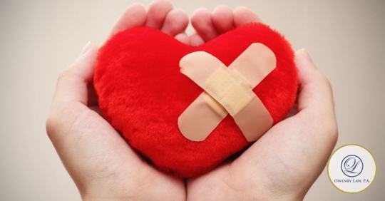 Plush heart with two adhesive bandages forming an "X" in a person's hands.